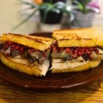 Grilled leftover turkey sandwich cut in half, showing layers of roasted turkey, savory stuffing, cranberry relish, and cheddar cheese.