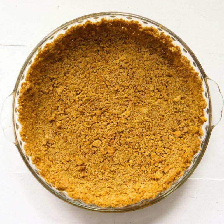 Homemade graham cracker crust with golden brown crumbs pressed into a clear glass pie dish.