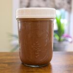 Homemade peppermint mocha coffee creamer in a glass jar with a white lid on a wooden table.