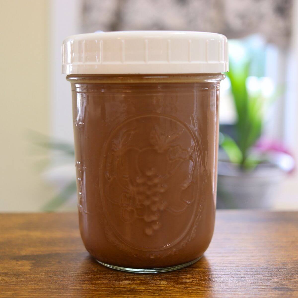 Homemade peppermint mocha coffee creamer in a glass jar with a white lid on a wooden table.