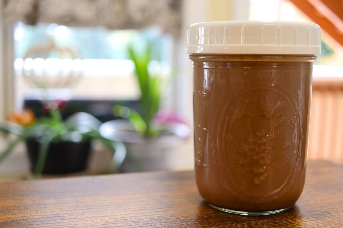 Glass jar filled with homemade peppermint mocha coffee creamer, sitting on a wooden table.