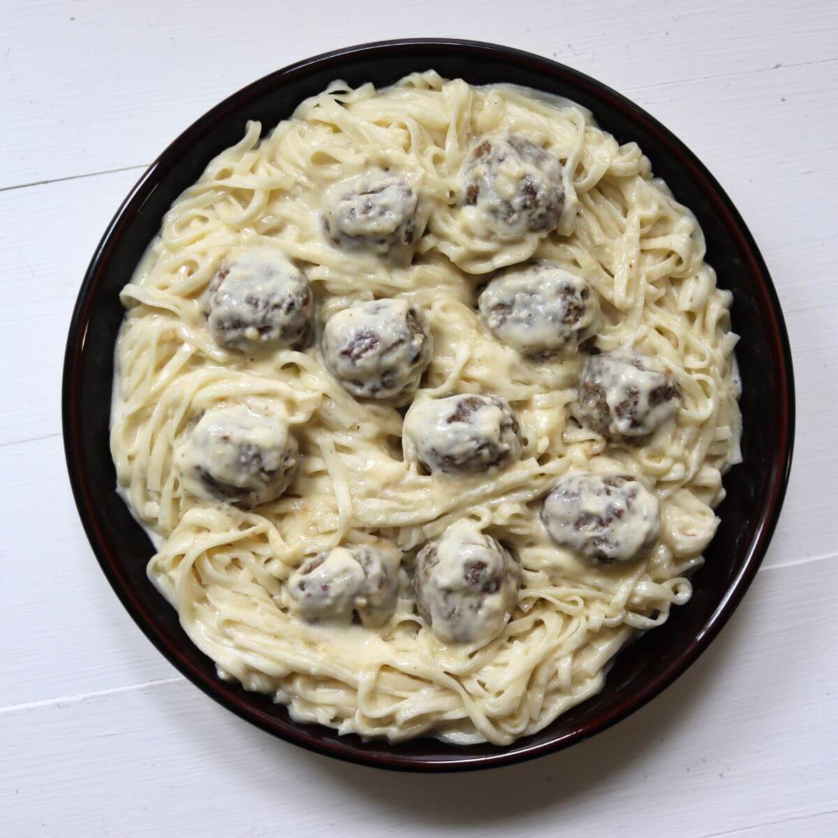 Homemade turkey meatballs nestled among flat noodles covered in Alfredo sauce.