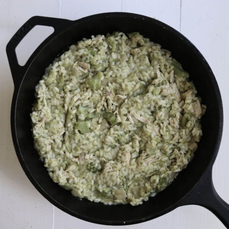Turkey risotto with shredded turkey, broccoli, and creamy Arborio rice filling a black cast iron skillet.
