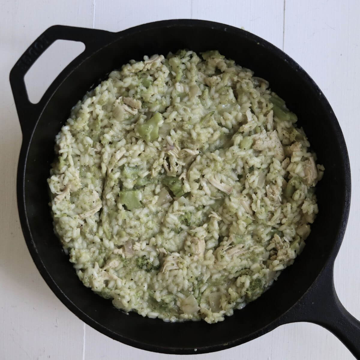 Turkey risotto with shredded turkey, broccoli, and creamy Arborio rice filling a black cast iron skillet.