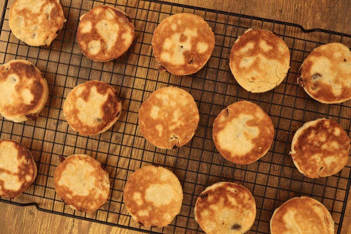 Welsh cookies with lightly crisp, golden surfaces arranged on a black wire cooling rack.