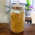 Wine sauerkraut with caraway seeds in a glass fermentation jar fitted with an airlock lid, sitting on a wooden table.